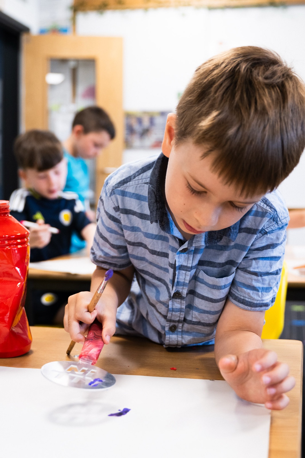 A schoolchild painting with an All In stencil during arts and crafts